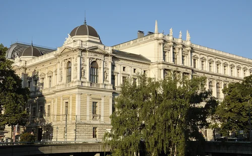 Pale historic façade with a dome and rooftop statues behind treetops