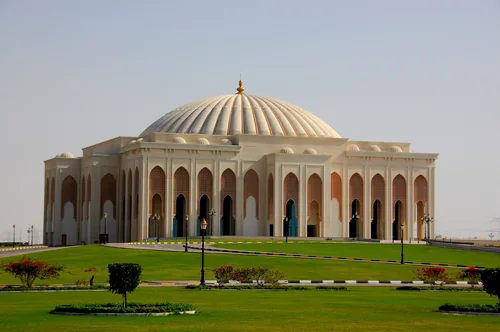 Building with a large ribbed dome and arches amid a lawn with flower beds