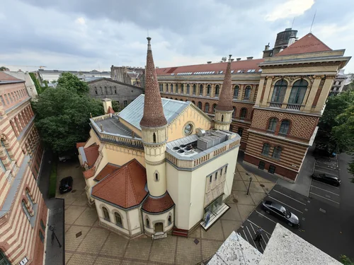 A view from above of a building with two pointed turrets and a tiled roof in a courtyard surrounded by striped-brick buildings