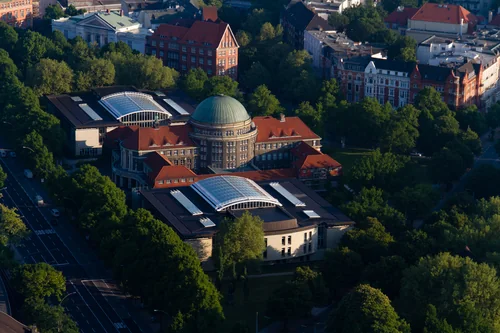 Aerial view of a building with a green dome and glass roofs among trees