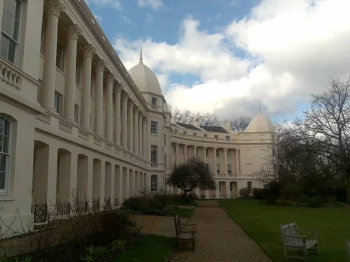 Curved cream façade with a colonnade and dome along a garden path with benches