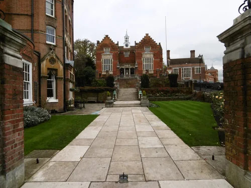 A paved path between lawns leading to steps and a brick building with stepped gables and a clock cupola
