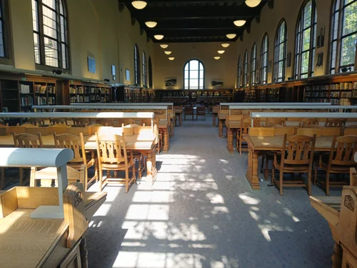 Empty reading room with wooden tables, bookshelves and tall arched windows