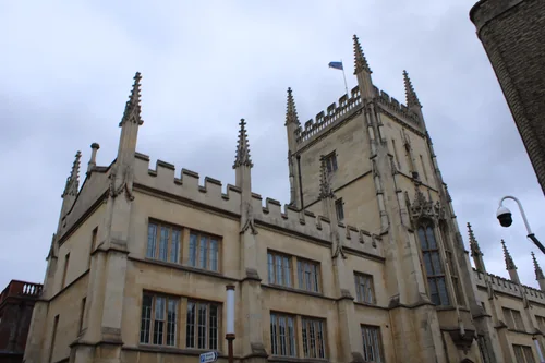 A Gothic Revival stone building with a tower, battlements and pinnacles, seen from below against a cloudy sky