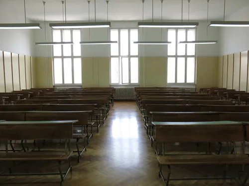 Empty classroom with wooden desks and three tall windows