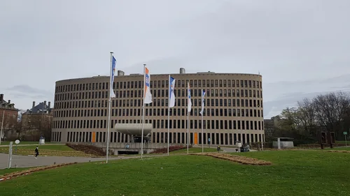 Rounded multi-storey building with flagpoles in front of a lawn