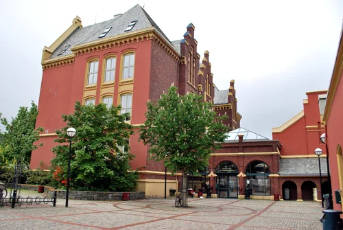 Red building with white windows and a stepped gable above a paved square