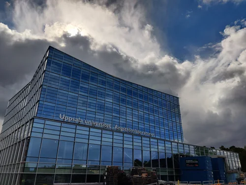 Glass building with the sign Uppsala universitet under a cloudy sky