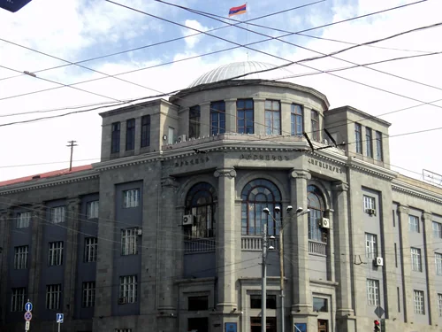 Grey stone building with a dome and a rounded corner façade under overhead wires