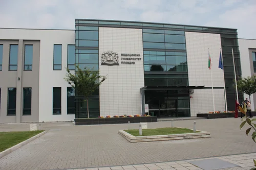 Modern building with a glass entrance and the university emblem, a paved square in front