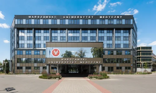 A modern glass building with the words Warszawski Uniwersytet Medyczny above the entrance, a paved walkway and flower beds in front