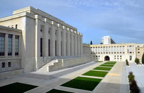 Massive pale stone buildings with a colonnade and broad steps, with strips of lawn in front