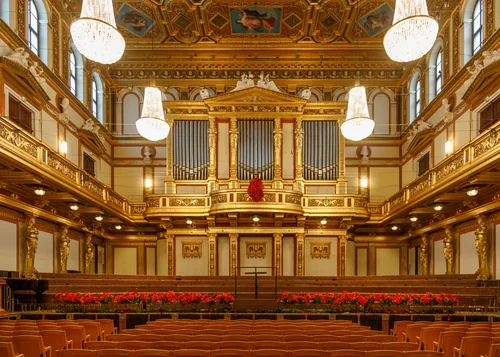 An empty concert hall with gilded walls, an organ, crystal chandeliers and rows of red seats