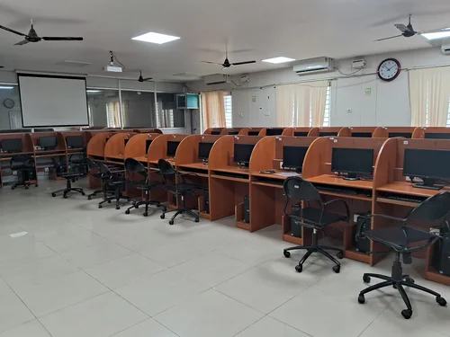 Rows of wooden carrel desks with monitors and black office chairs, a projector screen on the wall
