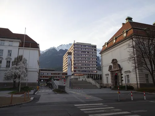 A street between historic university buildings, with a high-rise block and snowy mountains in the distance and a pedestrian crossing in the foreground