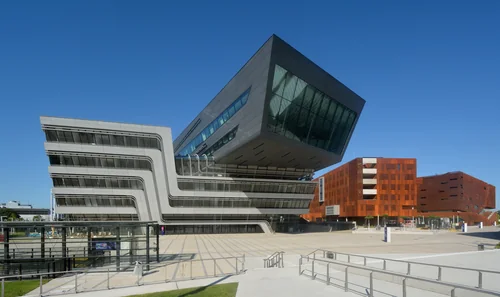 Futuristic building with a tilted dark volume next to a rust-red clad block