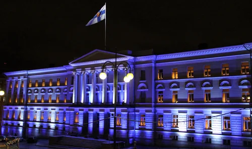A neoclassical building with a colonnade lit in blue at night, with glowing windows and street lamps