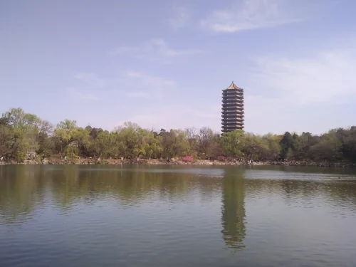 A multi-tiered pagoda above trees on the far shore of a calm lake, reflected in the water