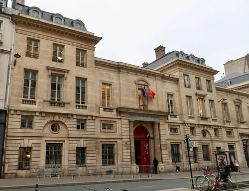 Classical stone façade with a red door, a SciencesPo sign and flags above the entrance