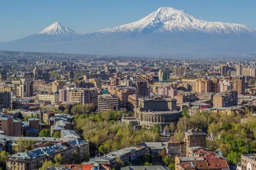 City panorama with the opera house among trees and two snow-capped peaks behind