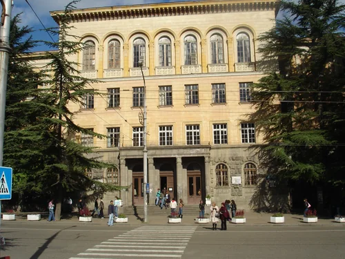 Yellow building with arched upper windows and an entrance colonnade behind a pedestrian crossing