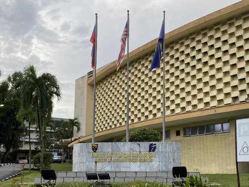 Building with a lattice facade, three flagpoles and a faculty sign in front