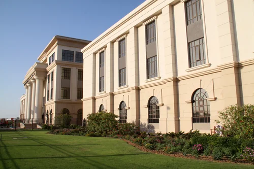 Pale building with columns and tall windows behind a lawn and flowering shrubs