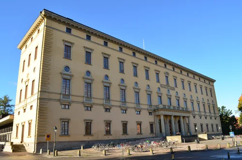 Long yellow building with rows of windows and bicycles by the entrance under a blue sky