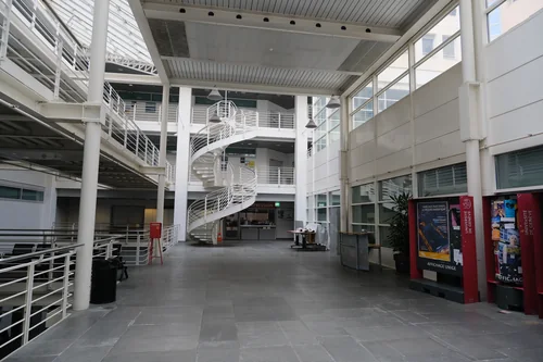 A bright multi-level atrium with a glass roof, white columns and a spiral staircase above an empty stone floor