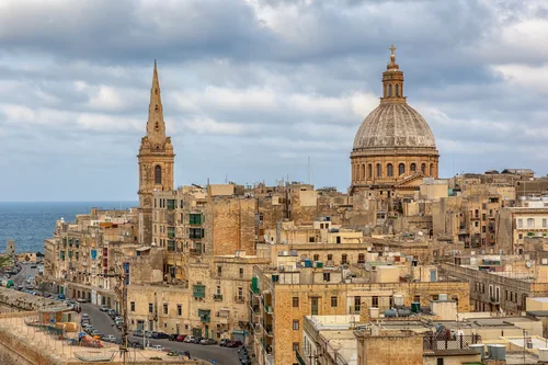 Dense sandstone buildings with a dome and a spire against the sea