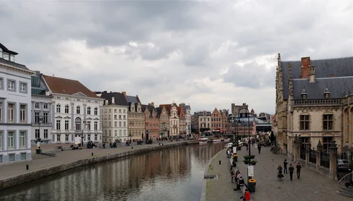 Historic facades along a canal and a quay with passers-by under a cloudy sky