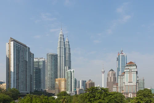 Skyscrapers with twin towers and a slender telecom tower above treetops