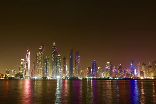Illuminated skyscrapers at night with colourful reflections in the water
