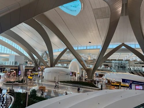 Spacious terminal hall with curved white supports, shops and a few passengers