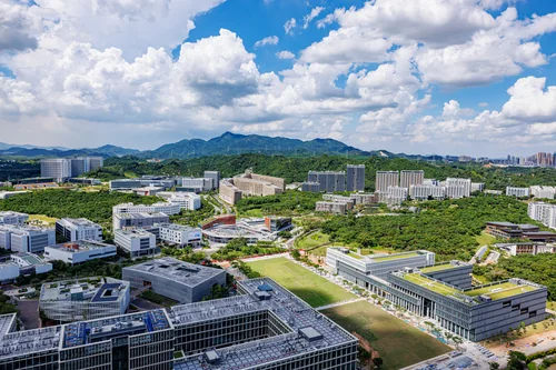 Aerial view of a modern campus among green hills under clouds