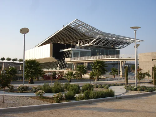 Building with a lattice steel roof among palms and flowering shrubs