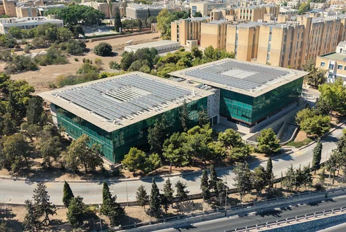 Aerial view of a glass building with rooftop solar panels among trees and limestone blocks