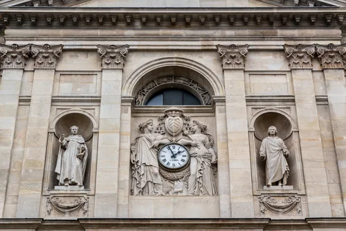 A stone façade with statues in niches, a clock flanked by two sculpted figures and Corinthian capitals