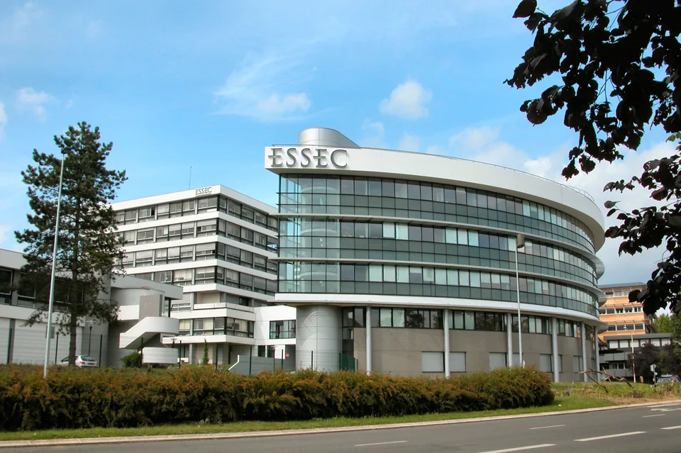 Полукруглый стеклянный корпус с надписью ESSEC рядом с белым многоэтажным зданием